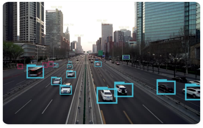 This image depicts a bustling urban highway integrated with AI-driven monitoring systems. Digital bounding boxes surround vehicles, including cars and a public bus, while floating data tags hover above the skyline. The scene illustrates a "smart city" infrastructure designed for real-time traffic management, automated surveillance, and enhanced transit efficiency through computer vision.